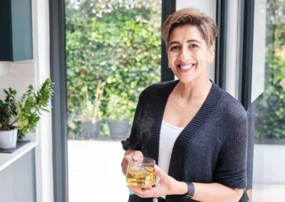 A creative natural portrait of a leading health practitioner holding a mug of herbal tea in her light and airy kitchen surrounded by plants and open space